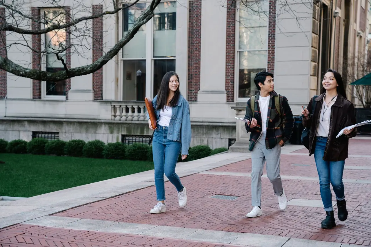 Group of young students walking on campus sidewalk on a bright day, showcasing casual university life.