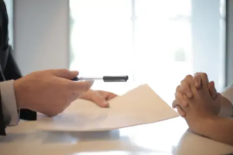 Side view of faceless formal man giving pen and paper to focused female with clenched hands at table on meetin