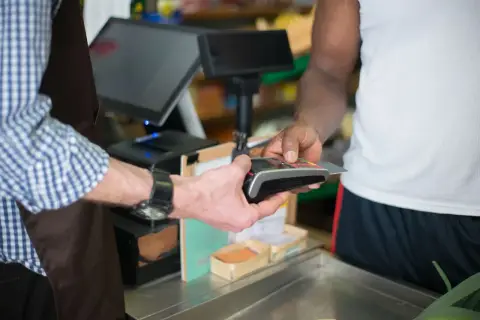 A customer making a payment with a credit card at a store checkout counter using a card reader.